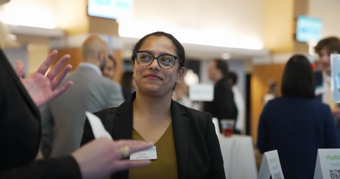 Student at recruiting event with glasses on smiling at someone off-camera.